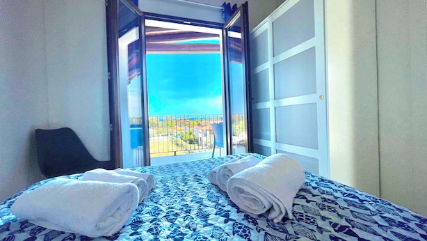 Une chambre d’hôtel avec un lit, deux serviettes, une chaise et une porte-fenêtre coulissante donnant sur un balcon avec vue.