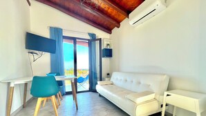 Un salon moderne avec un canapé blanc, une table à manger et des chaises, un téléviseur fixé au mur et un balcon avec vue.