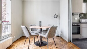 A dining area with a round table and four chairs, a floor lamp, and a view of a kitchen with appliances. - Blueground | Ternes, nr restaurants & attractions (Paris)