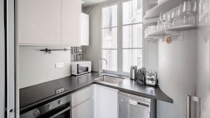 A modern kitchen with white cabinets, a built-in microwave, a coffee maker, and a dishwasher. - Blueground | Ternes, nr restaurants & attractions (Paris)