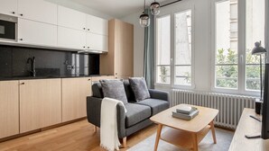 A modern kitchen with a grey sofa, a wooden coffee table, and large windows.