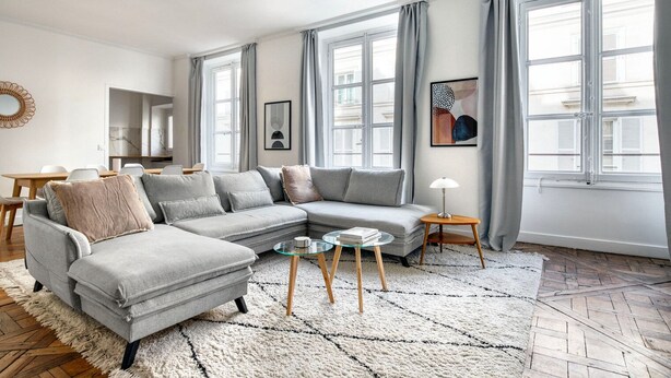 Un salon moderne avec un canapé d’angle gris, une table basse en verre et un tapis blanc.
