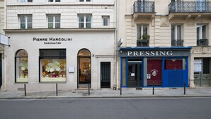 Une vue de rue avec des devantures de magasins, notamment celles de « Pierre Marcolini Chocolatier » et d’un pressing.