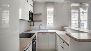 A modern kitchen with white cabinetry, a built-in oven, a sink, and a window overlooking a balcony.