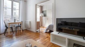 A modern living room with a sofa, TV, and dining area with chairs and a table. - Blueground | Auteuil, concierge, nr Seine & dining (Paris)