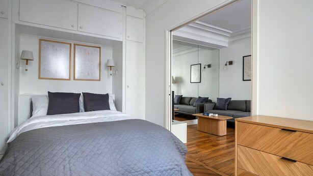A modern bedroom with a bed, a wooden dresser, a sofa, and a coffee table. - Blueground | Auteuil, concierge, nr Seine & dining (Paris)