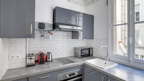 A modern kitchen with grey cabinets, a built-in microwave, a toaster, a kettle, and a sink. - Blueground | Auteuil, concierge, nr Seine & dining (Paris)