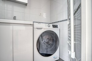Convenient laundry facility with a front-loading washing machine and storage cabinet.