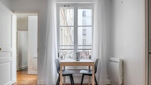 A room with a dining table and chairs, a radiator, and a window with curtains. - Blueground | Auteuil, concierge, nr Seine & dining (Paris)