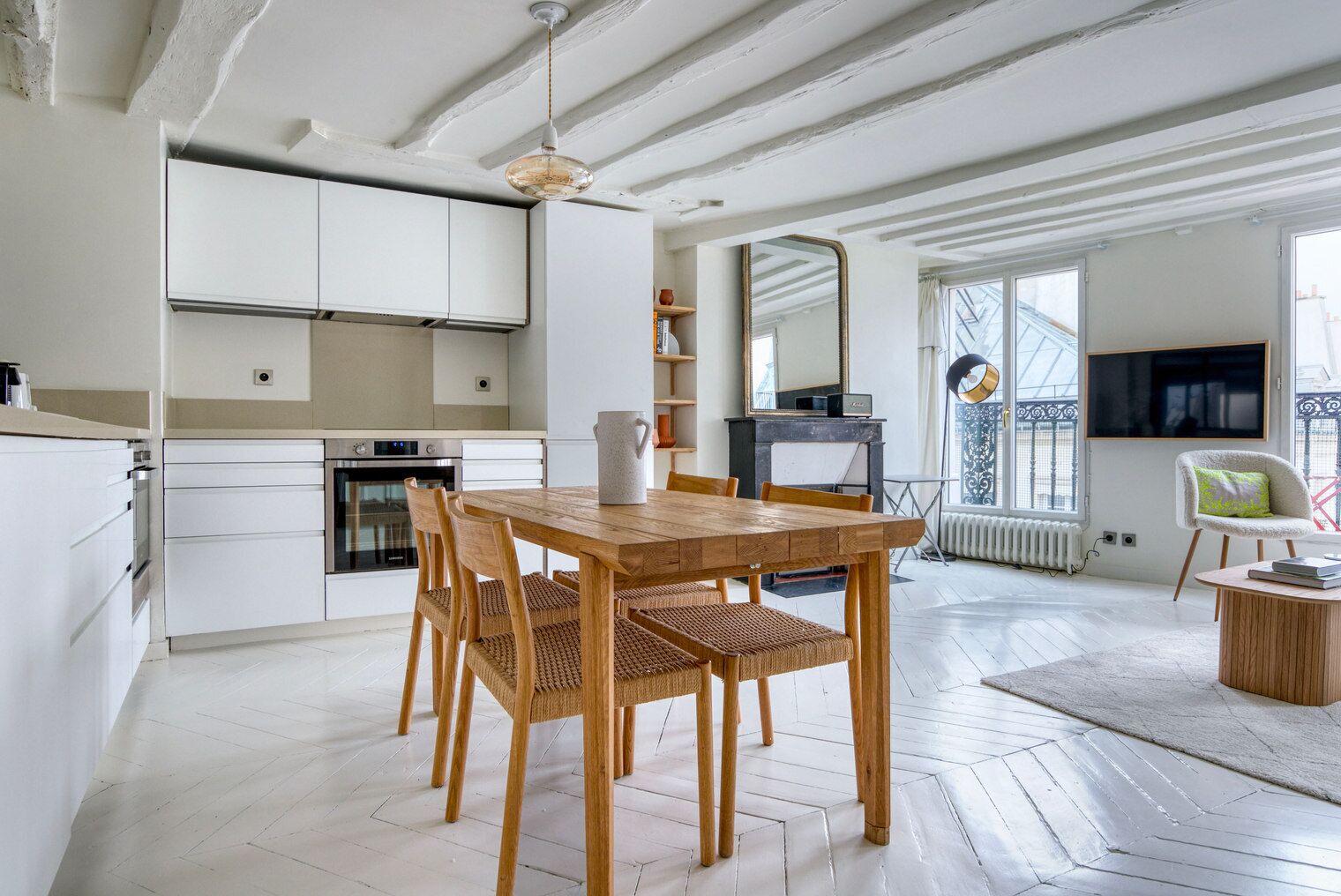 Una cocina moderna con armarios blancos, una mesa de comedor de madera y sillas de mimbre.