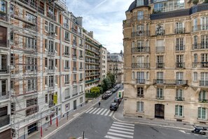 A multi-story urban street with buildings on either side, including a building with scaffolding and another with ornate architecture. - Blueground | Trocadéro, nr shops & Eiffel Tower (Paris)