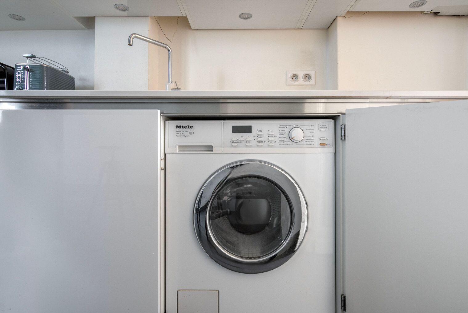 A compact, modern washing machine in a small laundry room with a simple design and minimal controls.
