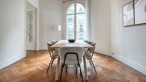 A dining room with a wooden table and chairs, a window with a view of buildings, and a door with a geometric design. - Blueground | Trocadéro, nr shops & Eiffel Tower (Paris)