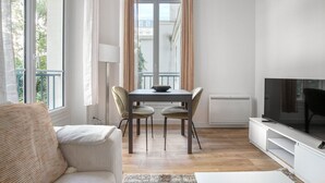A modern living room with a dining area, a flat-screen TV, and a view of the city through large windows. - Blueground | Miromesnil, nr offices & Monceau Park (Paris)