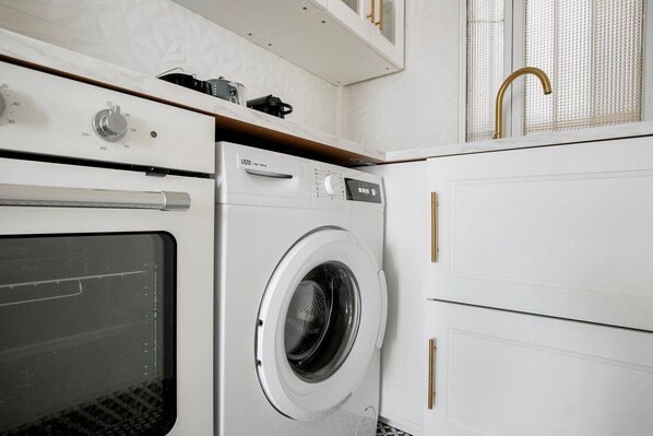 Une petite buanderie équipée d’un lave-linge, d’un four et d’un évier.
