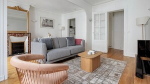 A modern living room with a grey sofa, a wooden coffee table, a pink chair, a fireplace, and a large mirror. - Blueground | Montmartre, close to shops & cafes (Paris)