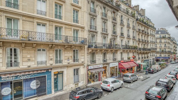 A row of multi-story buildings with various shops and a visible hotel sign. - Blueground | Montmartre, close to shops & cafes (Paris)