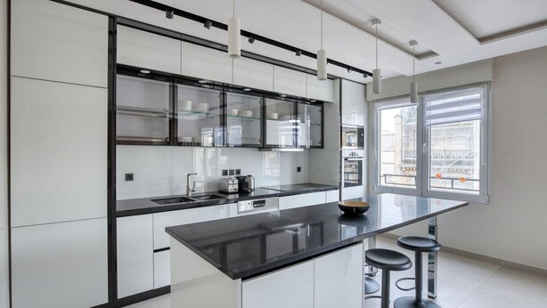 A modern kitchen with a black countertop, white cabinets, and a large window providing natural light. - Blueground | Mairie du XVI, balcony, nr dining (Paris)