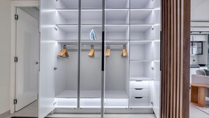 A walk-in closet with multiple shelves and hanging space, a sliding door, and a wooden accent wall. - Blueground | Mairie du XVI, balcony, nr dining (Paris)
