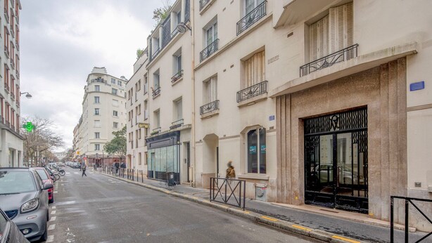 Une vue de rue avec une rangée d’immeubles à plusieurs étages, dont certains sont dotés de balcons et d’enseignes indiquant la présence de commerces.