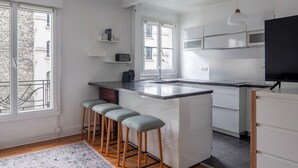 Une cuisine moderne dotée d’un îlot central, de tabourets de bar, d’un four à micro-ondes encastré et d’une grande fenêtre qui laisse entrer la lumière naturelle.