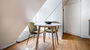 Een moderne loft slaapkamer met een schuine kap, een ronde eettafel, twee stoelen, een radiator en een garderobe.