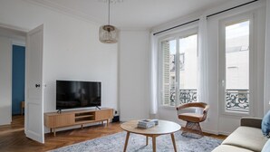 A modern living room with a flat-screen TV on a wooden stand, a round coffee table, a patterned rug, a sofa, and a chair. - Blueground | Pigalle, nr shopping & festive area (Paris)