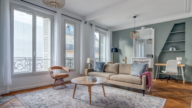 A living room with a sofa, a coffee table, a chair, and a desk with a lamp. - Blueground | Pigalle, nr shopping & festive area (Paris)