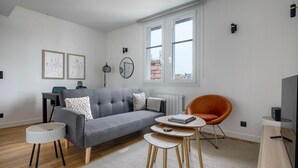 A modern living room with a grey sofa, a round orange chair, a small round table, and a TV stand. - Blueground | Sorbonne, balcony, a/c & great view (Paris)