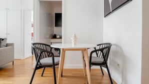 A modern living room with a round dining table, two black chairs, a grey sofa, and a kitchen in the background. - Blueground | Le Marais, elevator, close to market (Paris)