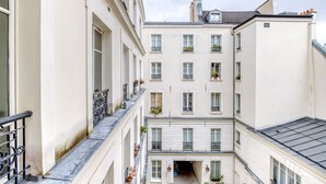 A narrow alleyway between buildings with balconies, a small courtyard, and a staircase leading to an upper floor. - Blueground | Le Marais, elevator, close to market (Paris)