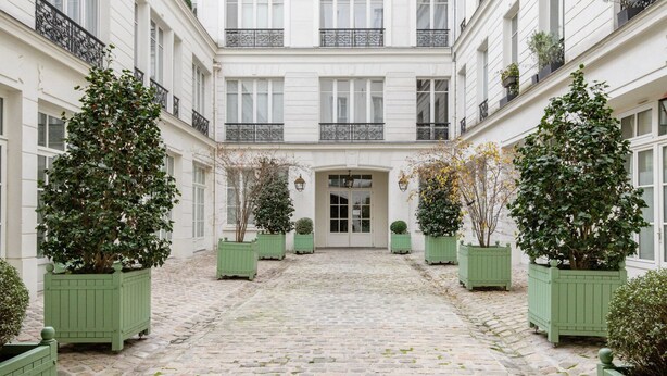 A courtyard with a cobblestone floor, surrounded by white buildings with balconies and green planters. - Blueground | Le Marais, elevator, close to market (Paris)