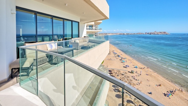 A modern hotel balcony with glass railings overlooking a beach and the sea.