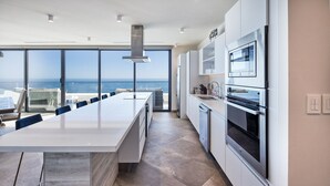 A modern kitchen with a large island, stainless steel appliances, and a view of the ocean.