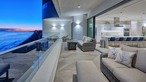 A modern outdoor living area with a glass balustrade overlooking a cityscape at dusk.