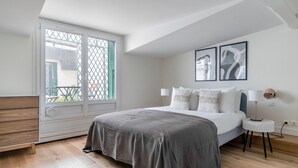 Une chambre à coucher avec un lit, une table de chevet, une lampe et une vue par la fenêtre.