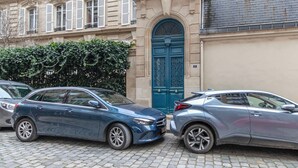 Deux voitures sont garées devant un immeuble dont la porte est bleue et la façade est en pierre.
