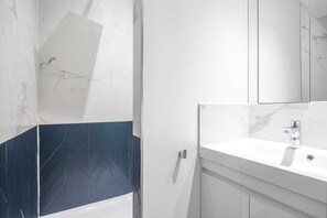 Une salle de bain avec un lavabo blanc, un miroir et un espace douche.