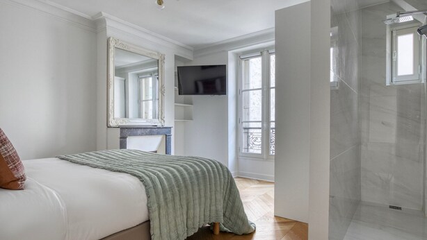 A bedroom with a bed, a television, a large mirror, and a shower area. - Blueground | Invalides, furnished, nr eiffel tower (Paris)
