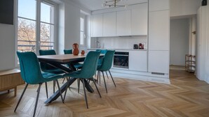 A modern kitchen with white cabinetry, a dining table with teal chairs, and a herringbone wood floor. - Blueground | Invalides, furnished, nr eiffel tower (Paris)