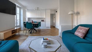 A modern living room with teal sofas, a coffee table, and a dining area with a kitchen in the background. - Blueground | Invalides, furnished, nr eiffel tower (Paris)