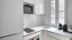 A modern kitchen with white cabinetry, a built-in oven, a microwave, a sink, and a window providing natural light. - Blueground | Bastille, nr shopping & dining (Paris)