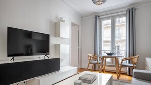 A modern living room with a flat-screen TV, a white coffee table, and a dining area with a table and chairs. - Blueground | Bastille, nr shopping & dining (Paris)