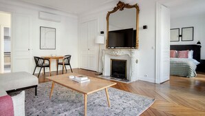 Un dormitorio moderno con chimenea, un espejo grande, una cama y un área de descanso con una mesa y sillas.