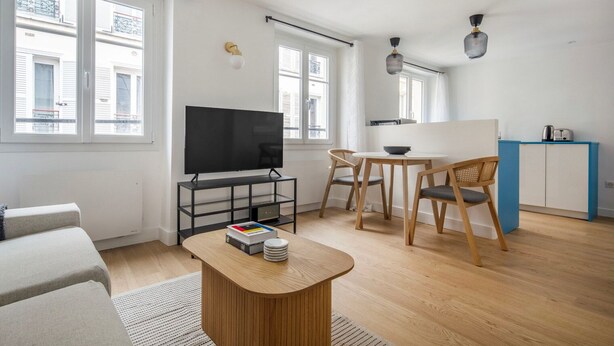 A modern living room with a flat-screen TV, a wooden coffee table, and a dining area with two chairs. - Blueground | Passy, walk to park & foodie area (Paris)