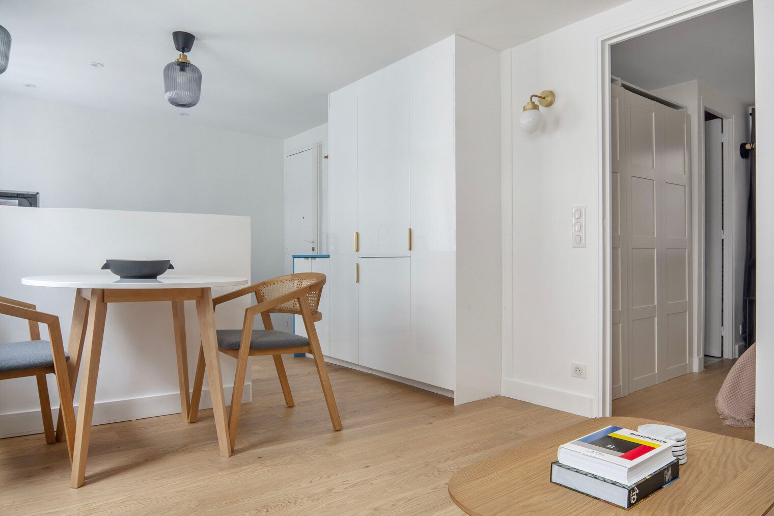 Una habitación moderna y minimalista con comedor, un armario blanco y una pequeña mesa con libros.