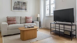 A modern living room with a sofa, coffee table, and a television on a stand. - Blueground | Passy, walk to park & foodie area (Paris)