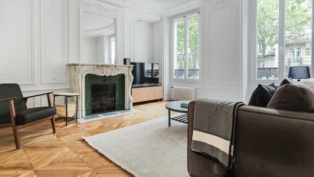 A living room with a fireplace, a sofa, a television, and large windows. - Blueground | Jardin du Luxembourg, walk to gardens (Paris)
