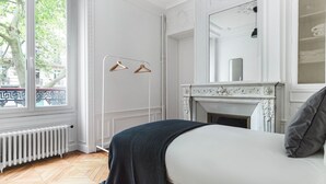 A bedroom with a bed, a radiator, a window with a view of trees, and a fireplace. - Blueground | Jardin du Luxembourg, walk to gardens (Paris)