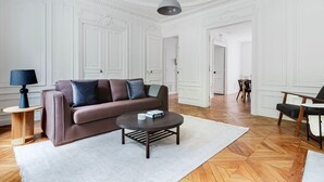 A spacious living room with a brown sofa, a round coffee table, and a modern pendant light. - Blueground | Jardin du Luxembourg, walk to gardens (Paris)